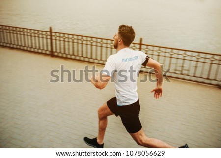 Photo from back of a young man running sprint in the morning around the lake.