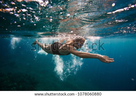 Professional female swimmer swim in the ocean on the sunrise, underwater picture