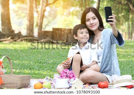 Family of mother and daughter son selfie take photo by camera of smartphone while a vacation picnic in a green grass park