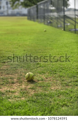 Looking through a deep blue wired fence, a green ball left on a softball playing field ready for a daily team practice with a long deep blue wired fence and a clear sky in summer time as background.