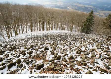 Stony hill. Mountain top in winter with snow and basalt stones. Misty forest and melancholy mood