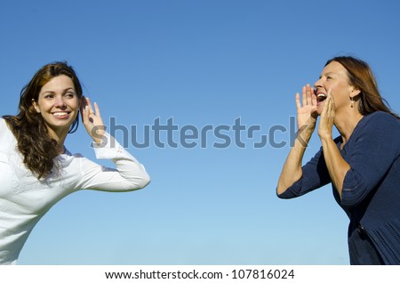 Two women, two generations, mother and daughter, two friends, communicating, one shouting, one listening, great distance, in front of a blurred green forest background Royalty-Free Stock Photo #107816024