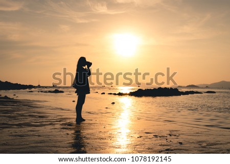 Silhouette of a young woman taking pictures of the sunset at koh lipe, Thailand in south east thailand.