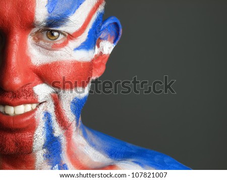 Man with his face painted with the flag of United Kingdom. The man is smiling and photographic composition leaves only half of the face.
