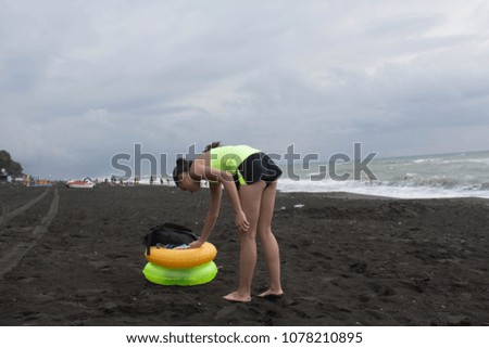 Girl and yellow, green Floating Ring on beach, overcast, clouds, waves. Travel or sea vacations concept