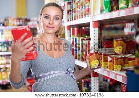 Cheerful  future mother is reading structure of product on shelves in supermarket