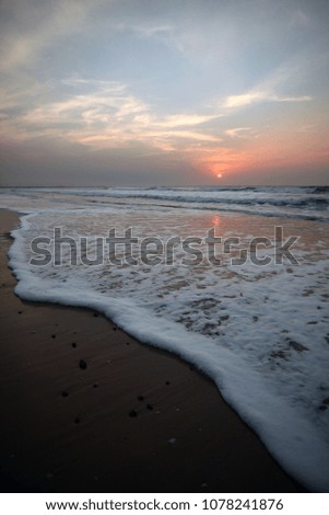 beautiful vertical wide angle sunset, at the Atlantic ocean, with wet flat sand, water waves and foam, with blue, purple, orange and yellow color, outdoors on a sunny day in the Gambia, Africa