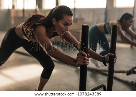 Strong young female pushing the prowler exercise equipment. Fit women exercising at gym.