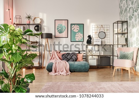 Knot pillow on a designer, emerald green mattress sofa in a living room interior with industrial furniture, a retro powder pink chair and plants Royalty-Free Stock Photo #1078244033