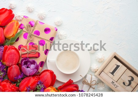 Multicolored tulips with gifts and coffee, and a calendar from May 13 on a light background, top view, with an empty space for writing or advertising. International Mother's Day