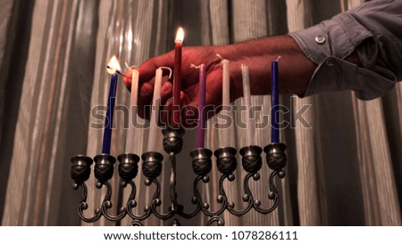 Old male hand lights candles on the seventh day of the Jewish holiday Hanukkah. 