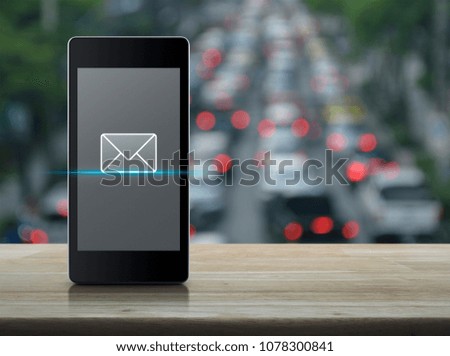 email icon on modern smart phone screen on wooden table over blur of rush hour with cars and road, Business communication concept