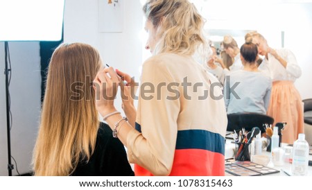 Rear view photo of makeup artist working with young model in studio