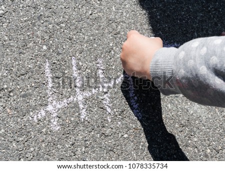 young girl hand holding thick chalk and writing her age on the street