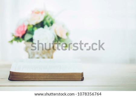 soft focus of open bible with blurred flowers vase over white background