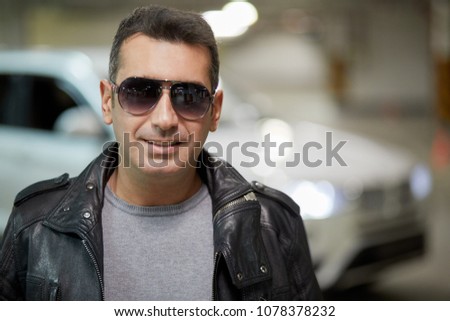 Portrait of man in dark sunglasses against white car at underground parking.