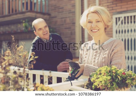 Mature smiling female talking with male neighbor at balcon