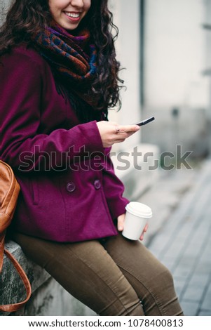 Girl standing agains t the wall on the street and using smart phone for texting.