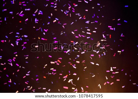 Thousands of confetti fired on air during a festival at night. Image ideal for backgrounds. Multicolor are the confetti in the picture. Magenta/purple/orange is the tonality of the background