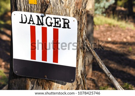 A danger sign with a unique design with black and red bright colors on a tree alerting mountain bikers and hikers of obstacles on the trail that may be a challenge and difficult to navigate