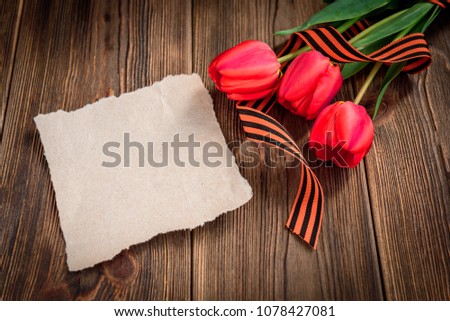 St. George ribbon, red tulips and paper greeting card on wooden background. Victory day or Fatherland defender day.