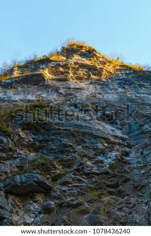 Low-angle view of a high steep rocky mountain with cliff illuminated by the sun