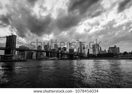 New York, USA. View of Manhattan bridge and Manhattan in New York, USA at sunset. Colorful cloudy sky with illuminated skyscrapers. Sun setting behind the skyscrapers. Black and white