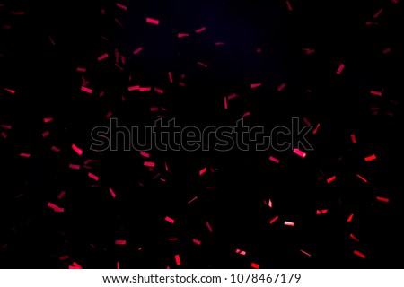 A few red confetti fired on air during a festival at night. Image ideal for backgrounds. Black sky as background. Confetti illuminated by lights
