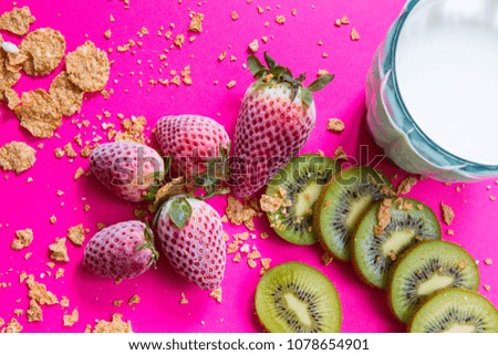 Bright breakfast picture: frozen strawberries, cut kiwi, spilled cereals and a glass of milk at fuchsia background