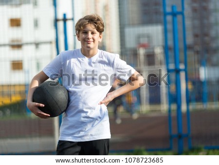 sporty, young, cute, healthy boy plays basketball on the sports playground at sunny summer day