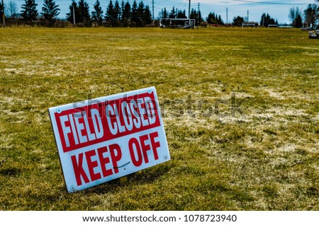 Sports field with a Closed, Keep Off  sign in the foreground on early spring grass