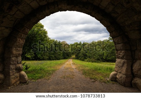 Old stone archway with dirt road leading into distant trees Royalty-Free Stock Photo #1078733813