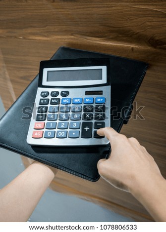 Female hand holding digital calculator on leather folder against wooden background