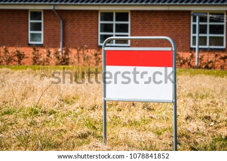 Real estate sign on a lawn in front of a red brick house with windows