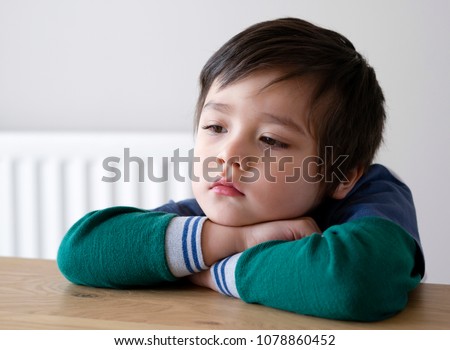 Lonely kid boy sitting alone and looking down with bored face, Closeup preschool child with unhappy or sad face, Head shot of bored 4-5 years old boy, Spoiled children concept