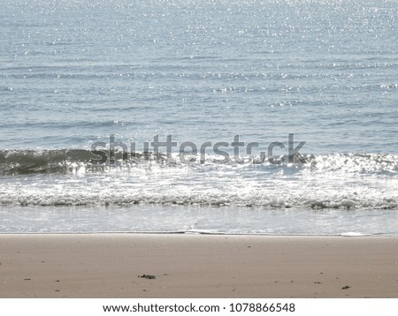 Sea waves blowing into the sandy beach with sunlight reflecting or sparkling glitter on water in the morning.