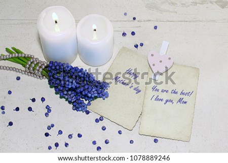Mother's Day, Women's Day or other suitable holiday card.
Background with two white burning candles, fresh blue muscaries bouquet and two old photo frames on vintage wooden planks. With text. 