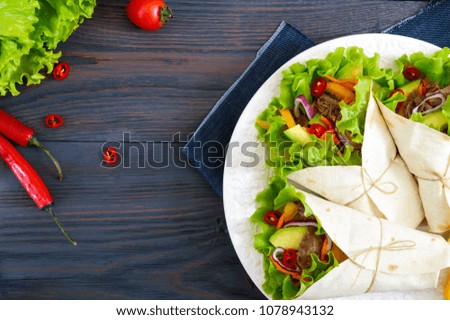 Burrito with chopped meat, avocado, vegetables, hot pepper on a plate on a dark wooden background. Stuffed tortilla. Traditional Mexican appetizer. Top view.