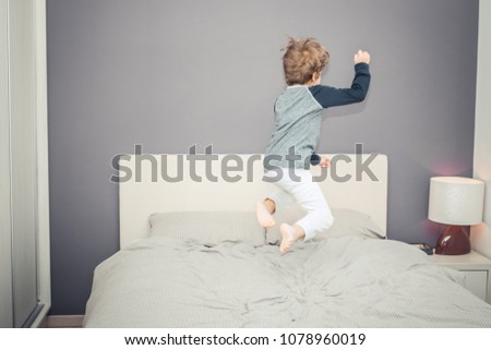 Back view of kid jumping high up on bed and having fun in the evening. Royalty-Free Stock Photo #1078960019