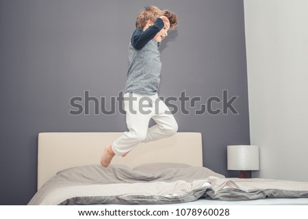 Playful boy in pajama jumping high up on the bed and having fun in the evening. Royalty-Free Stock Photo #1078960028