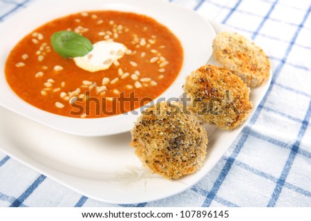 A picture of a white bowl full of fresh vegetable cream soup with pine nuts and three pieces of toast on side