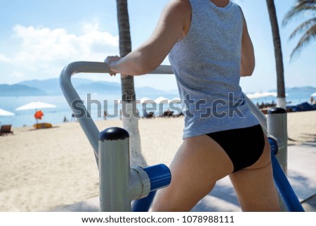 Woman training on simulator on sports ground against beach.Equipment for sports and healthy lifestyle.