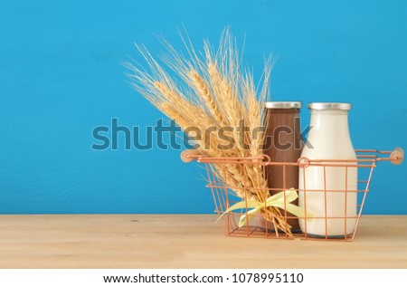 image of milk and Chocolate in the basket with wheat over wooden table and pastel background. Symbols of jewish holiday - Shavuot.