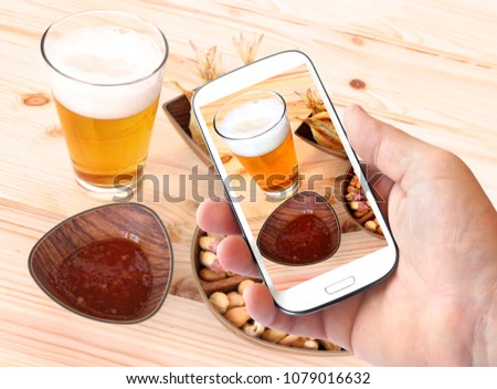 People use smartphone to take photos of beer and salt snacks - dry fish, nuts and spicy chili sauce on the rough wood