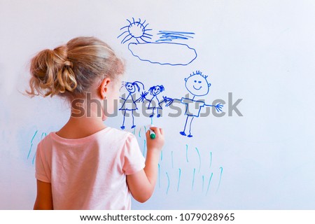 Little girl draws  family with marker on a white board: mom, dad and baby holding hands.