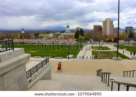 Salt Lake City, Utah State Capitol steps with the city skyline and a girl, a woman, in a red dress.  Looks like they were taking pictures of her in her prom dress.