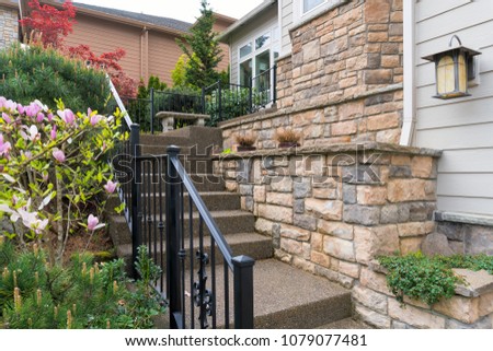 House front entry with concrete stairs iron rod railings stone wall planter siding by frontyard garden