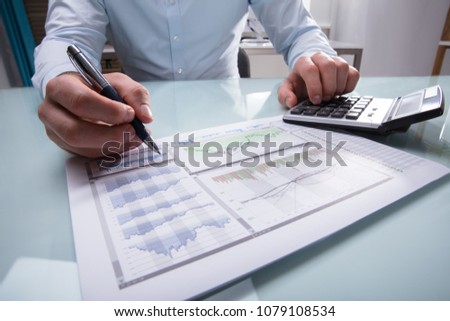 Photo Of Businessperson's Hand Analyzing Graph Using Calculator