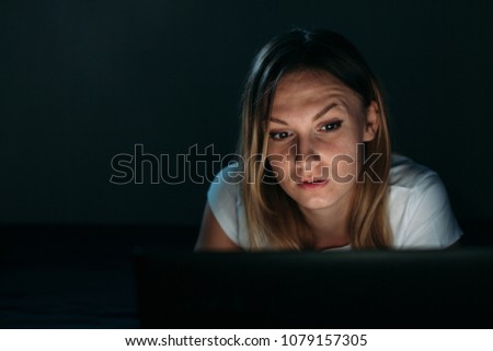 Lovely girl embarrassed by what she saw in the laptop. Night in badroom Isolated black. Front view. insomnia.