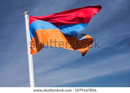 The national flag of Armenia, the Armenian Tricolour, flutters against the background of blue sky and white clouds.
